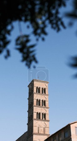 Photo for A serene bell tower rises elegantly against the blue sky, surrounded by the time-worn ruins of Rome's ancient landscape. It stands as a silent observer, witnessing the unceasing passage of time in a city steeped in history. - Royalty Free Image