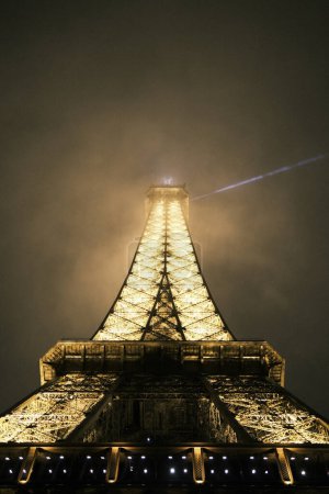 Foto de Pariss beloved Eiffel Tower pierces the night sky with its golden glow and shimmering lights, a sentinel of the city's endless charm and a beacon for romantics and dreamers. Iron lattice tower in its nightly splendor. - Imagen libre de derechos