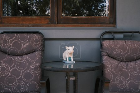 Photo for This charming image features a ceramic pig figurine poised on a round table between two patterned chairs on a cozy porch. The scene is a delightful representation of home decor and the personal touches that make a space feel welcoming. It's a snapsho - Royalty Free Image