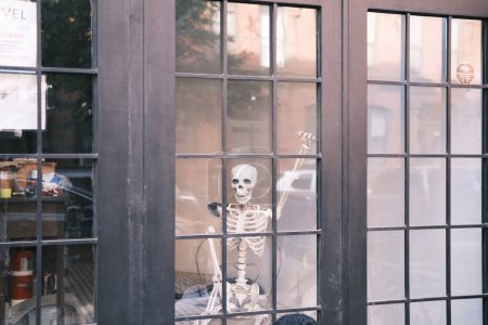 Photo for A humorous and slightly eerie scene unfolds in a New York City storefront window, where a skeleton with a guitar sits, offering a quirky take on urban life. - Royalty Free Image