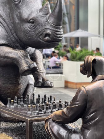 Téléchargez les photos : In the heart of New York City, an imposing rhinoceros sculpture encounters a focused chess player, in a scene where art meets life, creating an intriguing urban tableau. - en image libre de droit