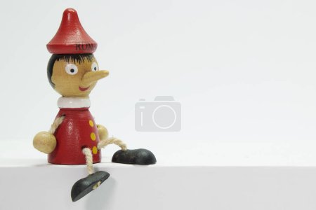 Téléchargez les photos : Pinocchio, jouet en bois représentant un garçon au long nez, assis sur un fond blanc uni et isolé. - en image libre de droit