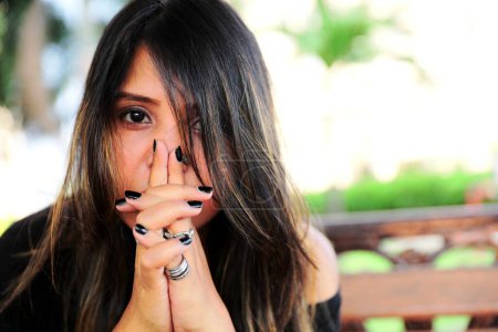 Portrait of a young woman with her hand partially covering her face showcasing stylish rings with a blurred background.