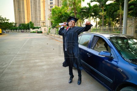 Graduate jumping and celebrating diploma, Next to car with degree, Student bounce off, Men frisk, jump joy in black cap gown, stands holding, A joyful expression, tall buildings, Indian, 30s, Asian.