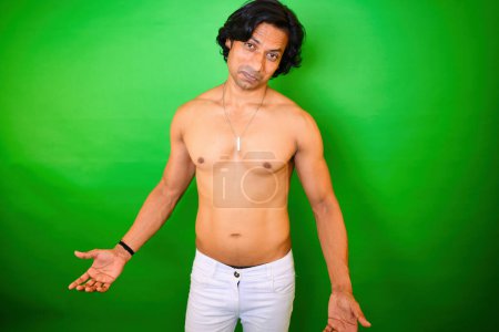 Shirtless man with expressive look posing, Stands against a green background, wearing white pants and necklace, He has an eloquent looks on his face, and his arms are outstretched, Indian, 30s Asian.