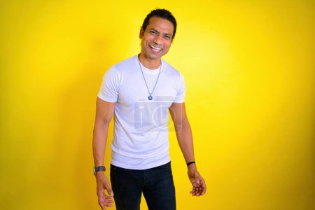 Laughing madly in studio, Man in white t shirt laughing against a yellow background. expressing happiness. toothy smile. Dental care. Indian. Laughter dental concept. Man enjoying success, Asian, 30s