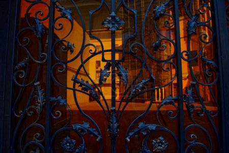 Beautiful, forged gate with many curls and leaves.Through the gate you can see the courtyard, illuminated by sunlight.