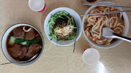 Top view of beef brisket noodle, century egg with cucumber and tofu, and sour and spicy pulled noodle