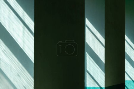 Foto de La luz del sol fluye a través de vidrio desigual en ventanas que proyectan sombras rayadas en paredes interiores verdes - Imagen libre de derechos