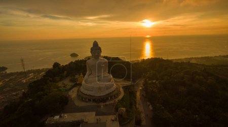 Foto de Vista aérea Phuket gran Buda en hermosa puesta de sol. El sol increíble brilla a través de las nubes amarillas impacto en la superficie dorada del mar. La belleza de la estatua encaja perfectamente con la naturaleza encantadora.. - Imagen libre de derechos