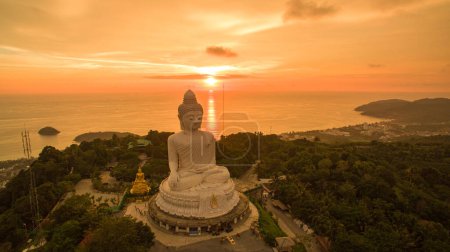 Foto de Vista aérea Phuket gran Buda en hermosa puesta de sol. El sol increíble brilla a través de las nubes amarillas impacto en la superficie dorada del mar. La belleza de la estatua encaja perfectamente con la naturaleza encantadora.. - Imagen libre de derechos