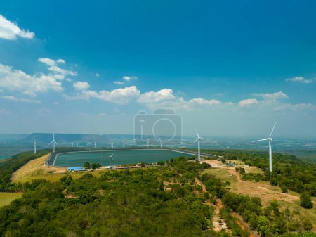 Téléchargez les photos : Vue aérienne des nuages blancs dans le ciel bleu au-dessus des éoliennes sur le sommet de la montagne dans le barrage de Lam Takong, Nakhon Ratchasima, Thaïlande. L'énergie éolienne produit de l'électricité. Énergie propre. - en image libre de droit