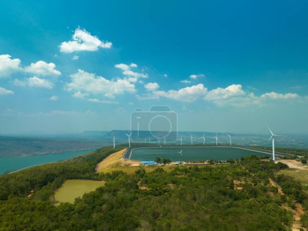 Téléchargez les photos : Vue aérienne des nuages blancs dans le ciel bleu au-dessus des éoliennes sur le sommet de la montagne dans le barrage de Lam Takong, Nakhon Ratchasima, Thaïlande. L'énergie éolienne produit de l'électricité. Énergie propre. - en image libre de droit