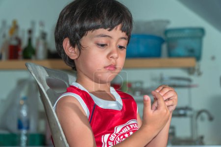 Photo for Asian little boy wearing red t-shirt sitting in the kitchen waiting for a meal - Royalty Free Image