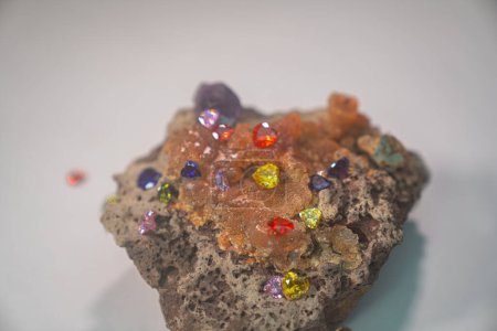 Foto de Diamantes coloridos en forma de corazón engastados sobre una piedra preciosa de ópalo en bruto sobre un fondo blanco - Imagen libre de derechos