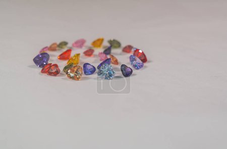 Photo for Beautiful multi-colored heart-shaped diamonds set in a circle.Heart-shaped diamonds in various colors are set on white floor.The sparkling light of diamonds looks charming and beautiful. - Royalty Free Image