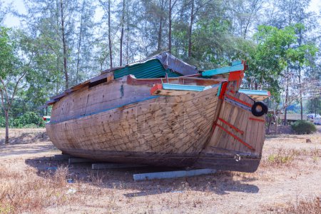 Photo for An ancient tugboat built of wood on the beachAn ancient tugboat built of wood on the beach..A large wooden boat is displayed on the beach with a blue sky. .Line of pine trees along the beach background. - Royalty Free Image