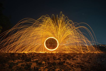 Photo for Reflection of spark fire swirl from steel wool with long exposure speed motion abstract at twilight on the sea. - Royalty Free Image