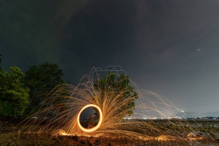 Téléchargez les photos : Réflexion d'étincelles tourbillonnant de laine d'acier avec une longue vitesse d'exposition abstraite au crépuscule sur la mer. - en image libre de droit