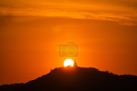 Téléchargez les photos : Décor Le soleil tourne derrière le Bouddha sur la montagne. Les nuages flottent paresseusement dans le ciel, et les rayons du soleil brillent du paysage environnant. le soleil descend lentement vers les montagnes. - en image libre de droit