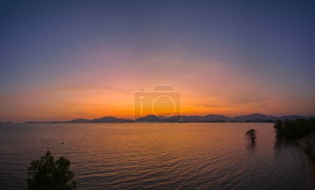 Foto de Cielo anaranjado al atardecer sobre el mirador Khao Khad Phuket. Hermoso El resplandor del sol brillaba a través de los manglares. Reflejos del sol en los manglares en la orilla del mar de los manglares. - Imagen libre de derechos
