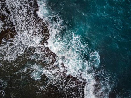 Foto de Una enérgica escena oceánica con olas chocando contra una costa rocosa. El mar en sí está coloreado con diferentes tonos de azul-verde con espuma blanca notable formada por las olas que no descansan. - Imagen libre de derechos