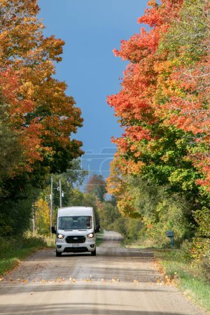 Téléchargez les photos : Ford transit conduite sur une route de campagne entourée d'arbres d'automne colorés. - en image libre de droit