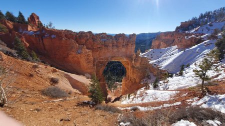 Photo for This stunning photo captures a natural rock arch in Bryce Canyon National Park, Utah. The red rock formation stands out against the snow-covered landscape and blue sky. - Royalty Free Image