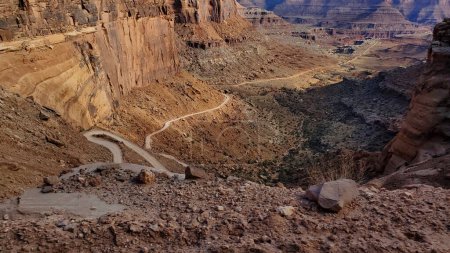 This stunning photo captures the rugged beauty of Shafer Switchbacks in Moab, Utah. The winding road cuts through the red rock canyon, offering breathtaking views of the desert landscape. 