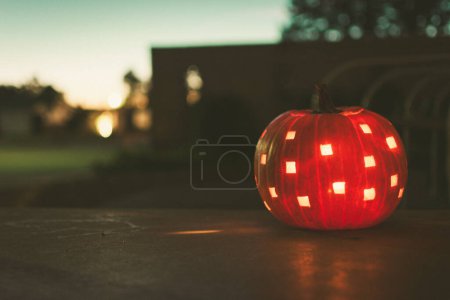Téléchargez les photos : Une lanterne Jack o 'éclairée assise sur un porche près de la nuit un soir d'automne, avec un fond flou, et une esthétique vintage. - en image libre de droit