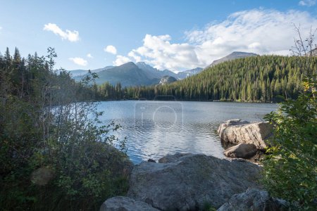 Téléchargez les photos : Après-midi soleil brillant sur un lac alpin entouré d'arbres et de montagnes à feuilles persistantes avec ciel bleu et nuages blancs. Vue sur le lac Bear dans le parc national des Rocheuses dans le Colorado. - en image libre de droit