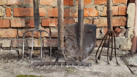 Foto de Viejas herramientas de jardín. diferentes sucia horquilla oxidada, pala, rastrillo y azada en el fondo de la pared de ladrillo. herramientas y equipos agrícolas - Imagen libre de derechos