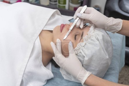 jeune femme couchée sur une civière dans un centre esthétique effectuant beauté faciale et traitement esthétique avec dermapen et scalpel techniques dermaplaning