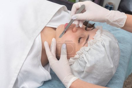 young woman lying on a stretcher in an aesthetic center performing facial beauty and aesthetic treatment with dermapen and scalpel dermaplaning techniques