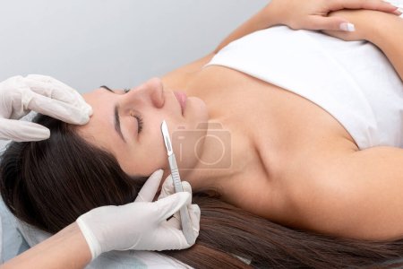 jeune femme couchée sur une civière dans un centre esthétique effectuant beauté du visage et du corps et traitement esthétique avec dermapen et techniques dermaplaning avec scalpel
