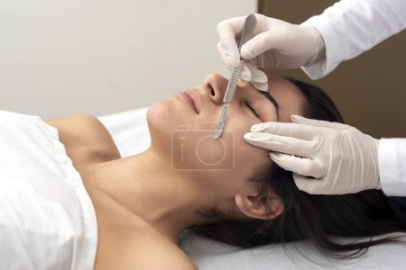 jeune femme couchée sur une civière dans un centre esthétique effectuant beauté du visage et du corps et traitement esthétique avec dermapen et techniques dermaplaning avec scalpel