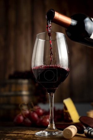 Foto de Copa de vino tinto con una botella de vino en una mesa de naturaleza muerta con abrelatas de madera de uvas y copa de vino que sirve en tablas de madera. - Imagen libre de derechos