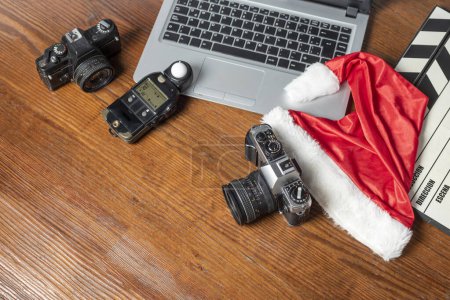 Téléchargez les photos : Appareils photo, planches à clins d'ordinateur et objets photographiques décorés d'un chapeau de Noël sur bois - en image libre de droit