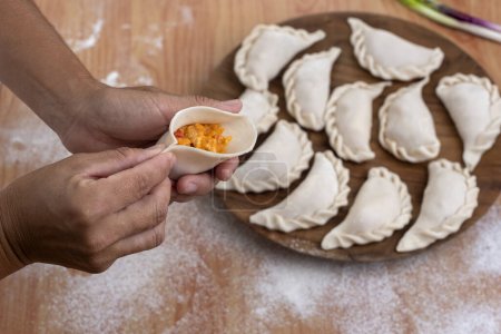 Photo for Process of making raw homemade empanadas with the dough and filling with hands assembling and filling the empanadas with vegetables meat chicken ham and cheese and making the repulgue - Royalty Free Image