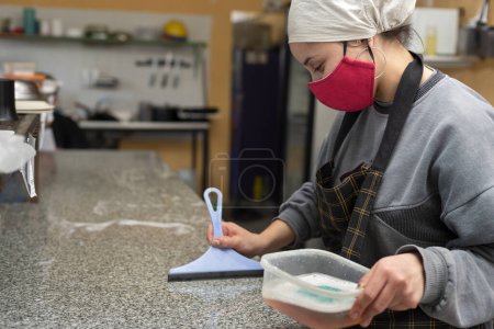 Téléchargez les photos : Deux jeunes entrepreneurs cuisinant dans une cuisine professionnelle avec gants et masque pour les soins d'hygiène alimentaire - en image libre de droit