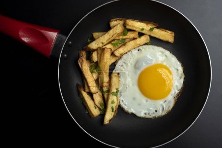 Téléchargez les photos : Oeuf frit aux pommes de terre dans une poêle noire au persil - en image libre de droit
