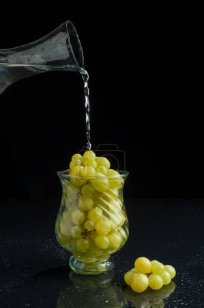 Téléchargez les photos : Raisins verts frais en grappe avec fond noir dans une tasse en verre - en image libre de droit