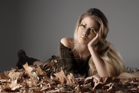 Téléchargez les photos : Jeune femme à l'automne regarder production avec des feuilles sèches d'un arbre qui représente la saison de l'année avec des couleurs brunes - en image libre de droit