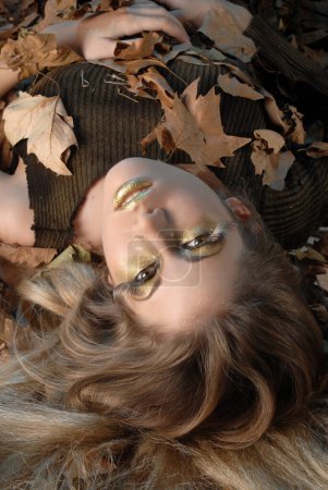 Téléchargez les photos : Jeune femme à l'automne regarder production avec des feuilles sèches d'un arbre qui représente la saison de l'année avec des couleurs brunes - en image libre de droit
