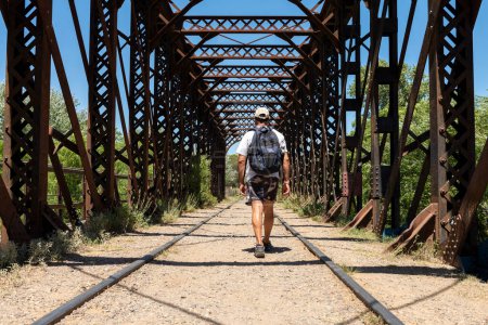 Photo for Man walking on an old iron bridge over the train tracks - Royalty Free Image