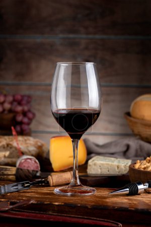 vaso de vino tinto con tabla de quesos pan de campo tabla de madera naturaleza muerta uvas frescas y botella
