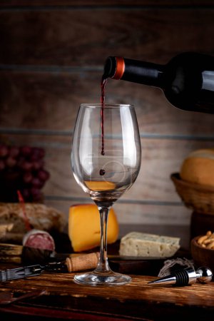 Téléchargez les photos : Verre de vin rouge avec plateau de fromage pain de campagne planche en bois nature morte raisins frais et bouteille - en image libre de droit