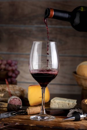Glas Rotwein mit Käsebrett Landbrot Holzbrett Stillleben frische Trauben und Flasche
