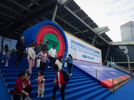 Téléchargez les photos : Shenzhen, Chine - 2 décembre 2023 : Les gens se tiennent devant un immense escalier bleu avec un grand bâtiment devant eux. Sous le cône, il est écrit "Salon mondial de l'alimentation 2023". Il y a aussi un signe de bienvenue sur les marches. - en image libre de droit