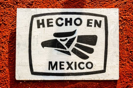 Foto de Foto de un cartel pintado a mano en blanco y negro, con el lema en español Hecho en México, sobre una pared roja. - Imagen libre de derechos